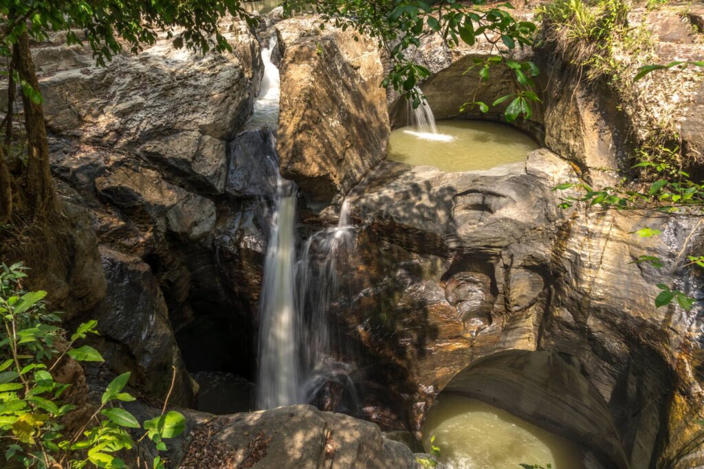 Emerald green river flowing between steep canyon walls at Cunca Wulang Waterfall in Flores