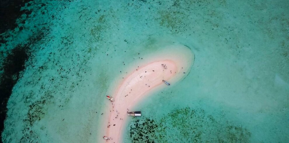 Aerial view of Taka Makassar’s crescent-shaped sandbar surrounded by turquoise waters