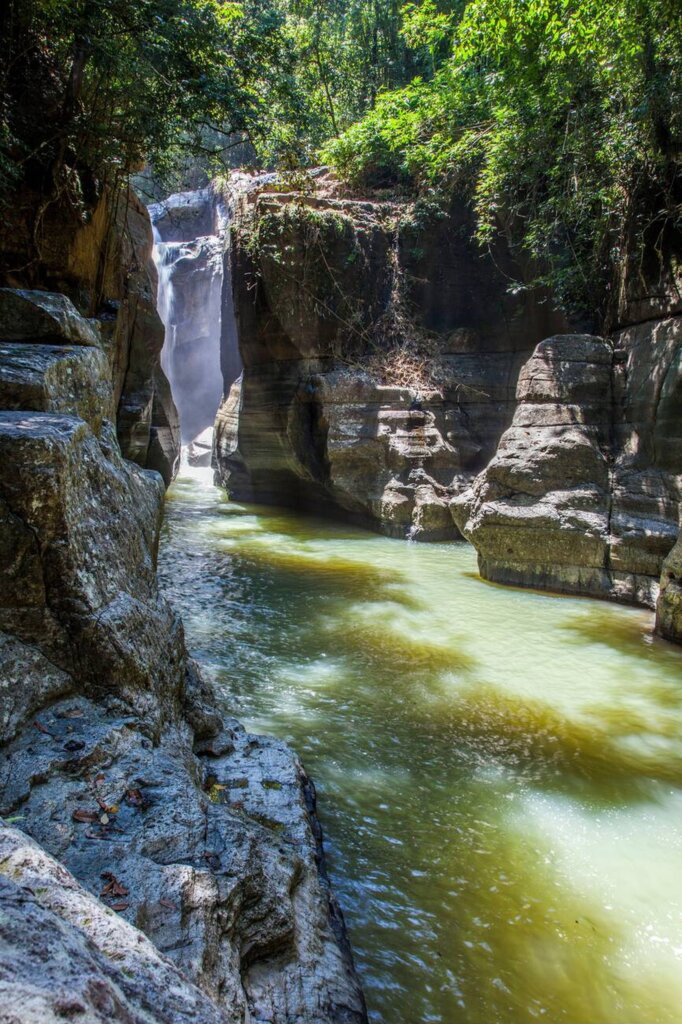 Emerald green river flowing between steep canyon walls at Cunca Wulang Waterfall in Flores