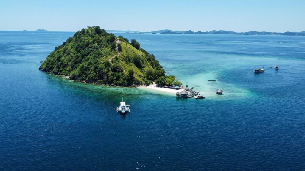 Aerial view of Kelor Island with its lush green hill and white sandy beach in Labuan Bajo